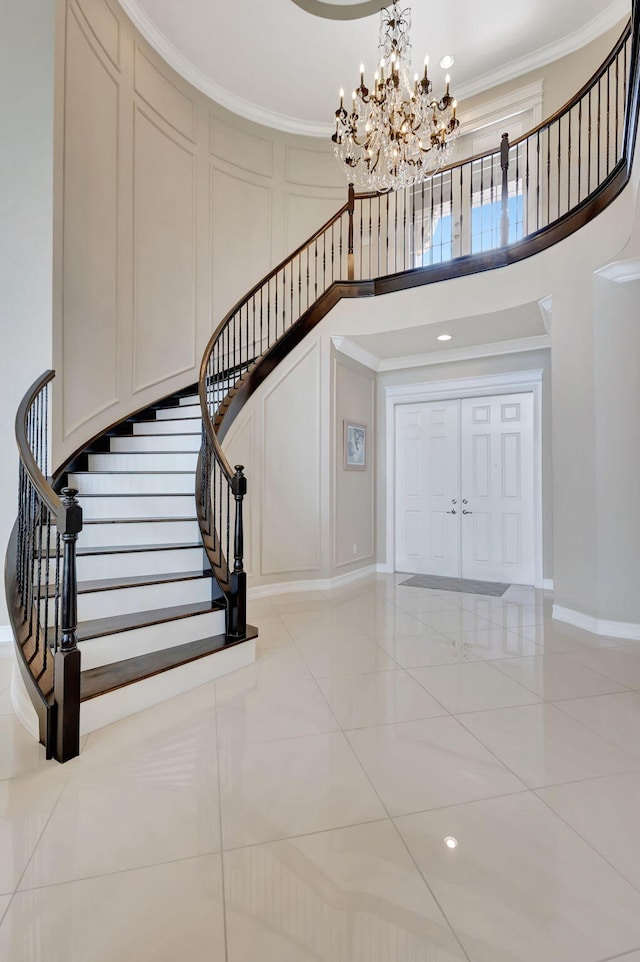 entryway with a decorative wall, crown molding, stairs, a high ceiling, and a notable chandelier