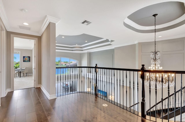 hall with a chandelier, wood-type flooring, crown molding, and a raised ceiling