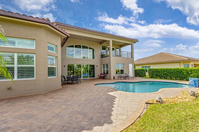 back of house featuring a balcony, a patio, a fenced in pool, and a lawn