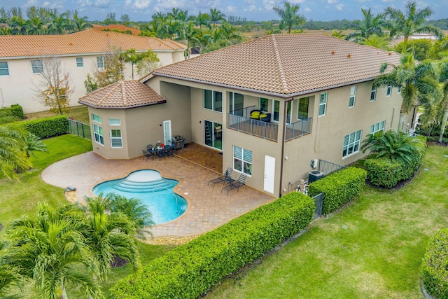 rear view of property with a patio, a balcony, cooling unit, a yard, and a fenced in pool