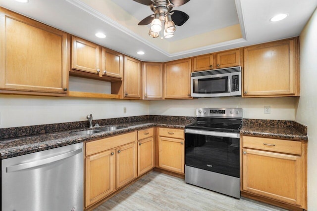 kitchen featuring sink, light hardwood / wood-style flooring, appliances with stainless steel finishes, a tray ceiling, and dark stone counters