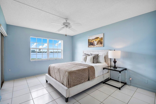 tiled bedroom with a textured ceiling, ceiling fan, and a water view