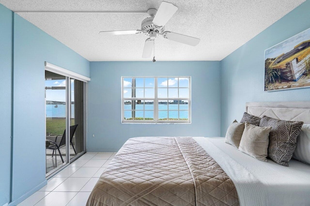 tiled bedroom featuring a water view, ceiling fan, multiple windows, and a textured ceiling