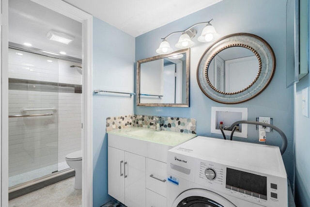 bathroom featuring vanity, washer / dryer, a shower with shower door, and toilet