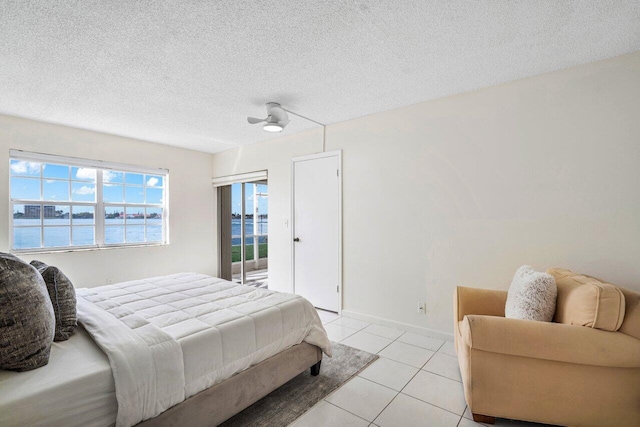 bedroom featuring a water view, ceiling fan, a textured ceiling, and light tile patterned floors