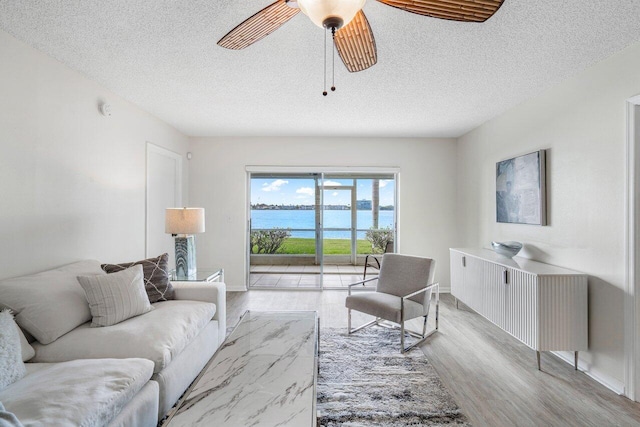 living room featuring ceiling fan, a water view, a textured ceiling, and light hardwood / wood-style floors