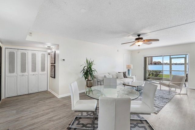 dining room featuring hardwood / wood-style floors, a textured ceiling, ceiling fan, and a water view