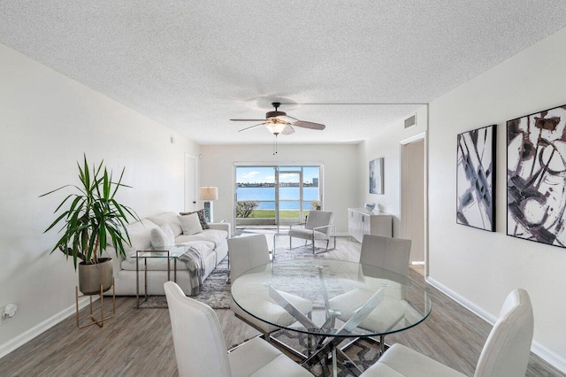 dining space with hardwood / wood-style flooring, ceiling fan, a water view, and a textured ceiling