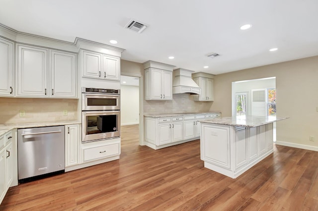 kitchen with a center island, light wood-type flooring, custom range hood, stainless steel appliances, and backsplash