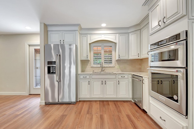 kitchen featuring appliances with stainless steel finishes, sink, backsplash, light stone counters, and light wood-type flooring