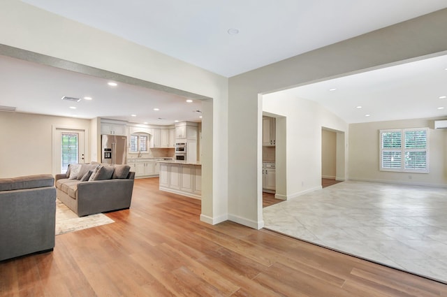 living room featuring lofted ceiling, light hardwood / wood-style flooring, and a wall mounted AC