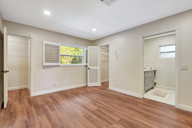 unfurnished bedroom with ensuite bathroom, a walk in closet, and light hardwood / wood-style floors