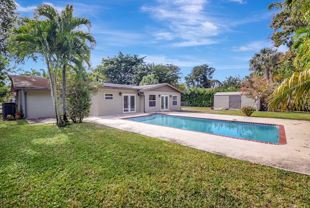 view of swimming pool with a lawn, french doors, cooling unit, a patio area, and a storage shed