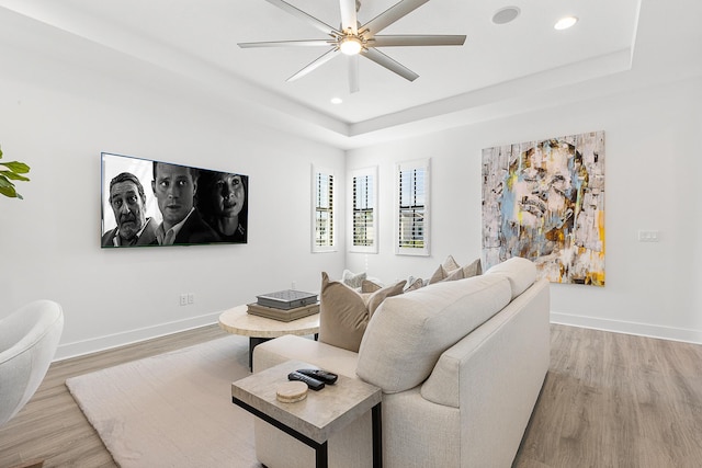 living room with ceiling fan, a tray ceiling, and light wood-type flooring