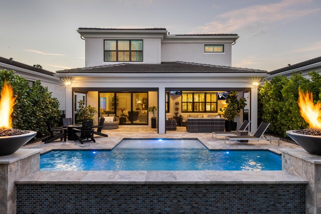 back house at dusk featuring a patio area and an outdoor living space with a fire pit