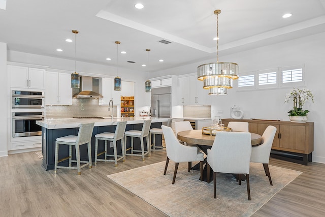 dining space with an inviting chandelier, a raised ceiling, and light hardwood / wood-style floors