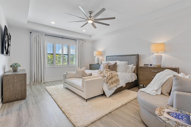 bedroom with a raised ceiling, ceiling fan, and light wood-type flooring