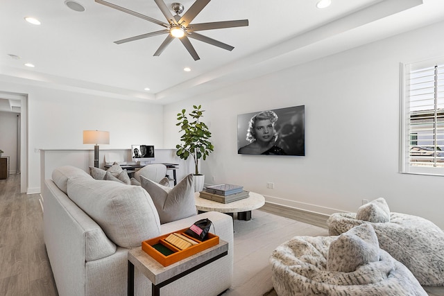 living room with ceiling fan, a tray ceiling, and light wood-type flooring