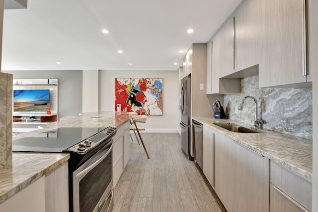 kitchen with sink, light hardwood / wood-style flooring, appliances with stainless steel finishes, light stone counters, and tasteful backsplash