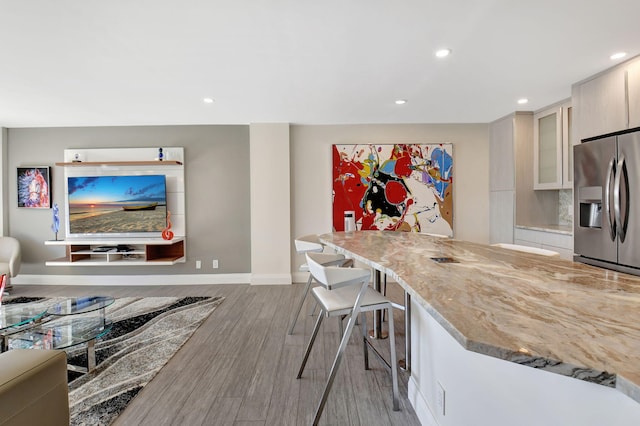 kitchen with light stone counters, a breakfast bar, stainless steel fridge with ice dispenser, and light hardwood / wood-style flooring