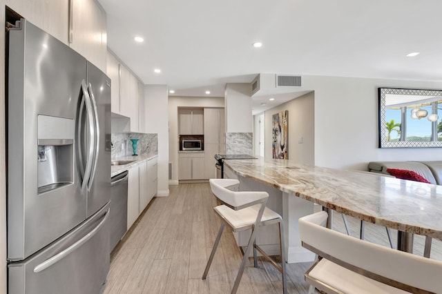 kitchen featuring tasteful backsplash, light stone countertops, stainless steel appliances, and light hardwood / wood-style floors