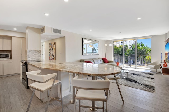 kitchen featuring electric range, a wall of windows, light stone countertops, light hardwood / wood-style floors, and decorative backsplash