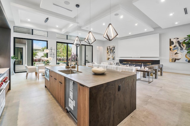 kitchen featuring an island with sink, a tray ceiling, sink, and decorative light fixtures