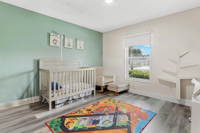 bedroom featuring a crib, wood-type flooring, and a textured ceiling