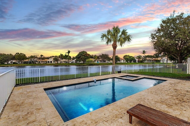 pool at dusk featuring a water view and a patio