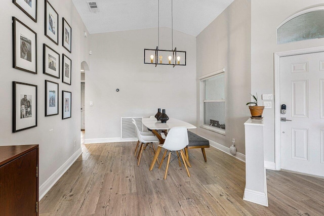 dining space featuring a textured ceiling, high vaulted ceiling, a chandelier, and light wood-type flooring