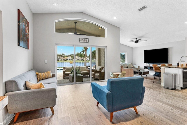 living room featuring vaulted ceiling, ceiling fan, light hardwood / wood-style floors, and a textured ceiling