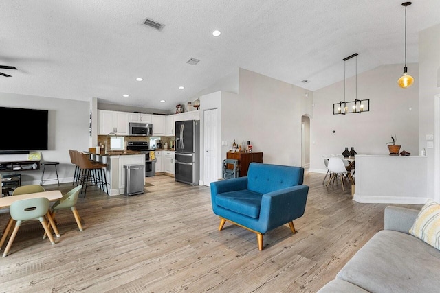 living room featuring an inviting chandelier, light hardwood / wood-style floors, vaulted ceiling, and a textured ceiling