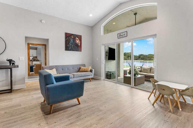 living room featuring high vaulted ceiling, a textured ceiling, and light hardwood / wood-style flooring