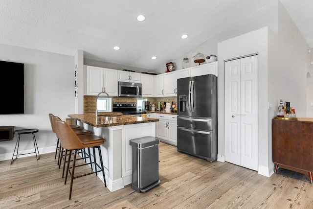 kitchen with a breakfast bar, appliances with stainless steel finishes, white cabinetry, tasteful backsplash, and kitchen peninsula