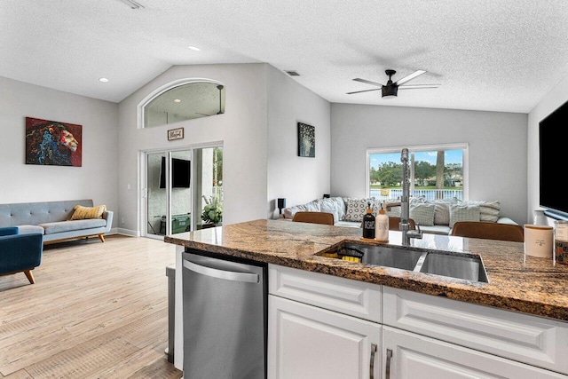 kitchen with vaulted ceiling, a textured ceiling, dark stone counters, light hardwood / wood-style floors, and white cabinets