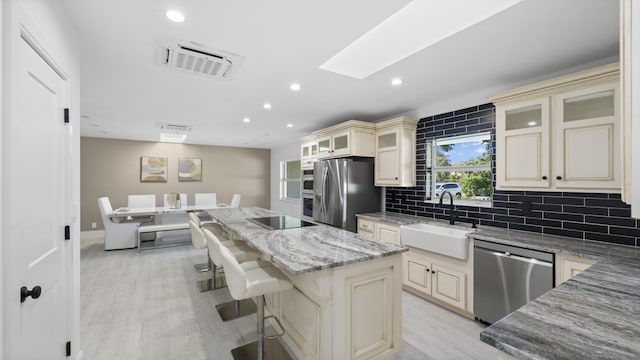 kitchen featuring sink, a kitchen breakfast bar, stainless steel appliances, a center island, and light stone counters