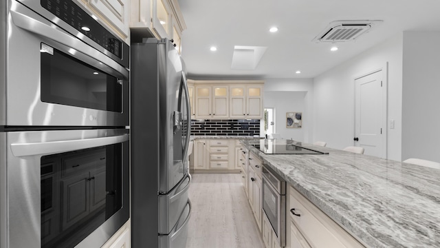 kitchen featuring appliances with stainless steel finishes, light stone counters, cream cabinets, tasteful backsplash, and light hardwood / wood-style floors