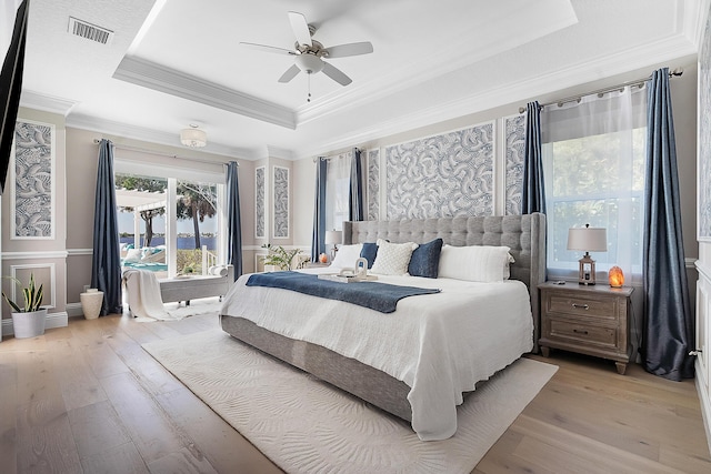 bedroom featuring visible vents, a raised ceiling, light wood-style floors, and ornamental molding