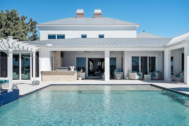 rear view of property with a patio, outdoor lounge area, metal roof, an outdoor pool, and a standing seam roof