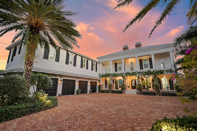 view of front facade with a standing seam roof, decorative driveway, a chimney, and stucco siding