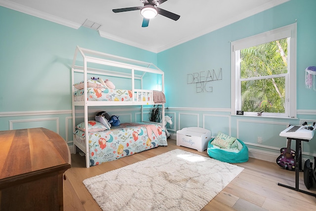 bedroom featuring visible vents, wainscoting, wood finished floors, and crown molding