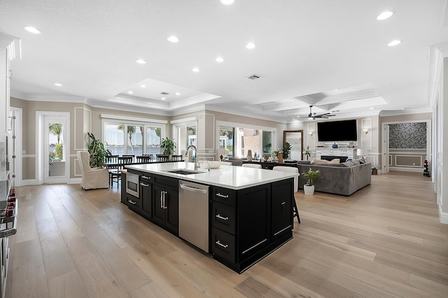 kitchen featuring a kitchen island with sink, ornamental molding, a sink, dark cabinetry, and stainless steel appliances