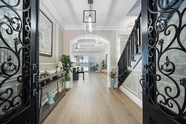 foyer entrance featuring stairway, a wainscoted wall, light wood-type flooring, ornamental molding, and arched walkways