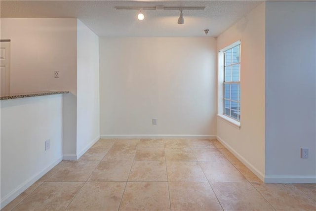 spare room with rail lighting, light tile patterned floors, and a textured ceiling