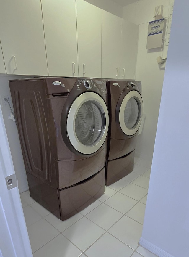 laundry area with independent washer and dryer, cabinets, and light tile patterned flooring