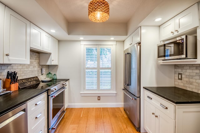 kitchen featuring light hardwood / wood-style flooring, backsplash, stainless steel appliances, white cabinets, and a raised ceiling