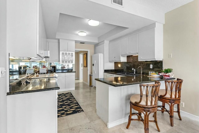 kitchen with sink, kitchen peninsula, white refrigerator with ice dispenser, decorative backsplash, and white cabinets