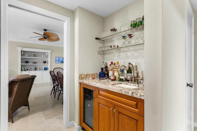 bar featuring sink, built in features, ceiling fan, and light stone countertops