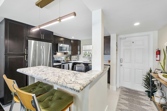 kitchen with pendant lighting, light stone countertops, a breakfast bar, and appliances with stainless steel finishes