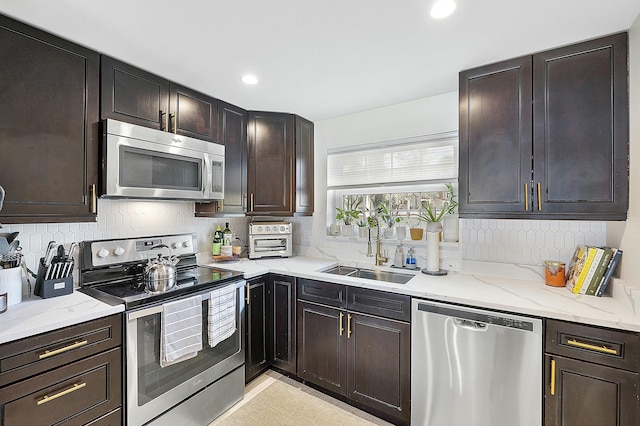 kitchen featuring sink, appliances with stainless steel finishes, backsplash, light stone counters, and dark brown cabinetry